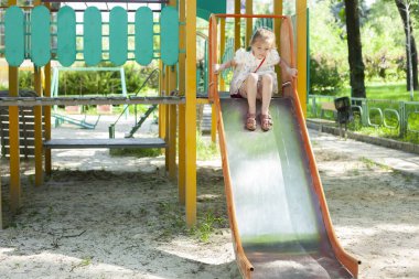 Parkta küçük bir kız oynuyor. Çocuk, çocukların kaydırağından kayıyor..