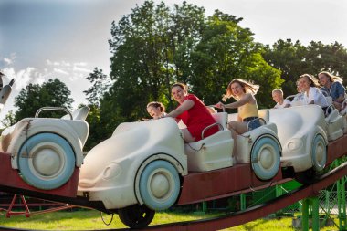 İnsanlar lunaparkta atlıkarıncaya biniyor. Çocuklu aileler atlıkarıncalarda eğleniyor.