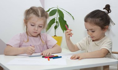 Genç bir anaokulu öğretmeni çocuklarla resim çizer. Anne ve kızları masada kalemle resim çizerler..