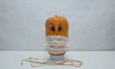 Beyaz arka planda tıbbi maske takmış korkunç bir balkabağı. Cadılar Bayramı kendini izole etme