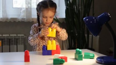 Küçük kız masadaki inşaatçıyı oynuyor. Çocuklar için eğitici oyunlar. Bir çocuk inşaatçıdan kule inşa eder..