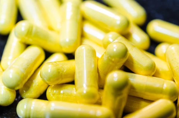 Yellow capsules macro closeup on black plate — Stock Photo, Image