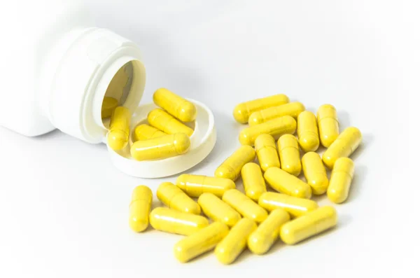 Yellow capsules pill spilled from white container — Stock Photo, Image