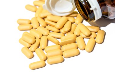 Piles of vitamin tablets drop from brown bottle isolated clipart