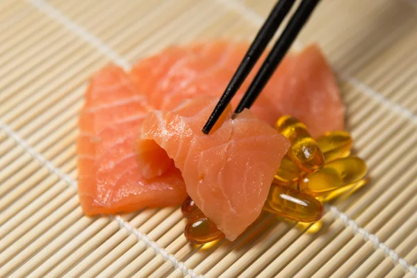 Lachs-Sashimi gemischt mit Fischöl-Kapseln mit Essstäbchengriff Stockbild