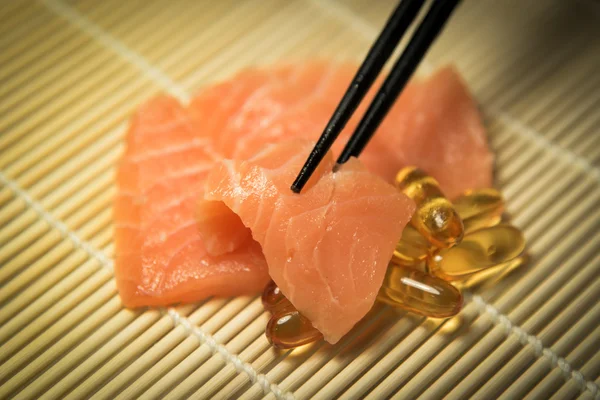 Сашими из лосося, смешанного с капсулами рыбного масла и палочками для еды — стоковое фото