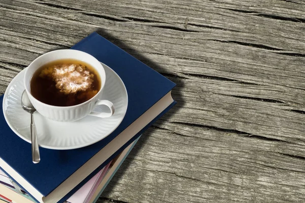 Bir fincan sütlü çay ve kitap yığını. Ahşap masa arkaplanı.