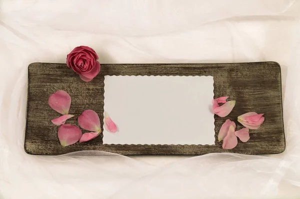 Tahta bir tabakta beyaz kağıt maketi. Pembe gül ve yapraklarla.