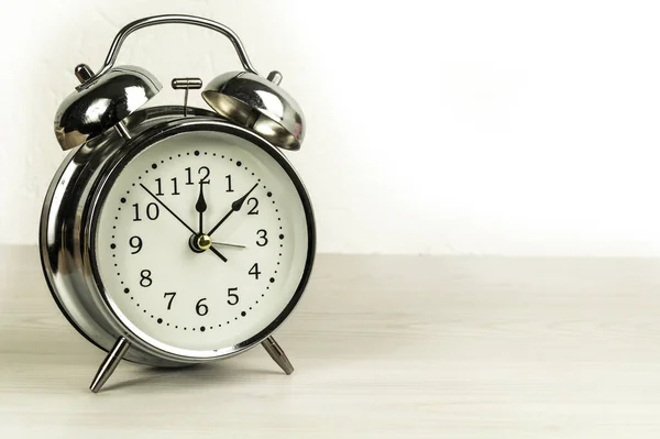Ahşap masa üzerinde beyaz arka planda gümüş retro alarm saati.