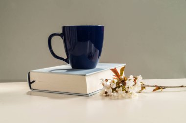 Kahve fincanı ve çiçek çiçekli kitap beyaz masada. Gri arkaplanlı.