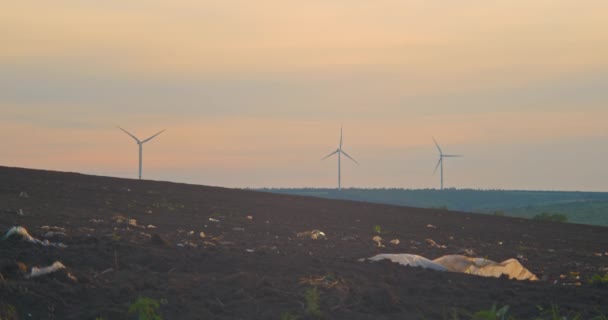 Ecologisch contrast: veld met plastic afval en windgeneratoren op achtergrond — Stockvideo