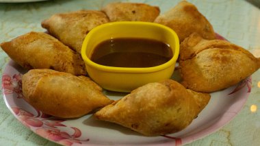 This is an Indian dish called samosa which is served on a white plate with sauce. All items or dishes are cooking at home