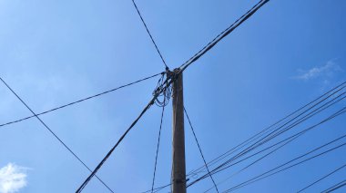 Parlak mavi gökyüzüne karşı elektrik kabloları ve beton kutuplar.