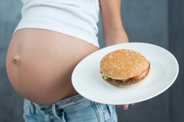 Close up of a cute pregnant belly and junk food. Hamburger and p — 스톡 사진