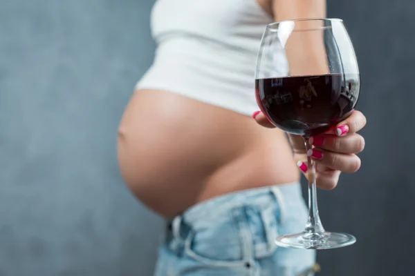 Close up of a cute pregnant belly and glass of wine. Alcohol and
