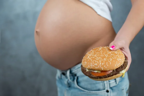 Close up of a cute pregnant belly and junk food. Hamburger and p