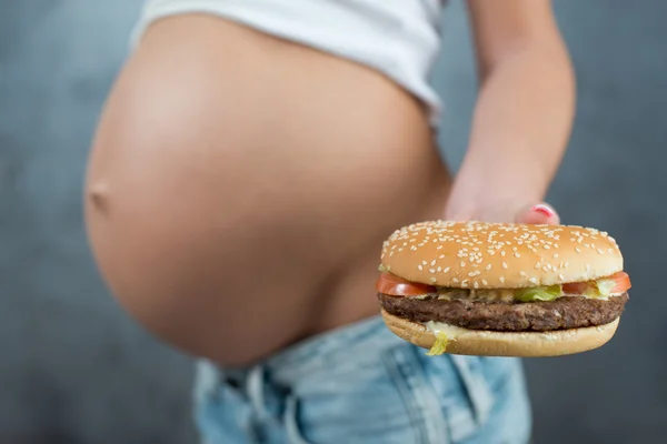 Close up of a cute pregnant belly and junk food. Hamburger and p — Stockfoto