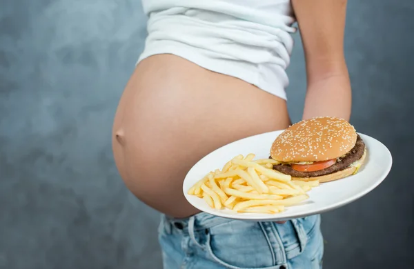 Close up of a cute pregnant belly and junk food. Hamburger and p