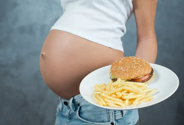 Close up of a cute pregnant belly and junk food. Hamburger and p