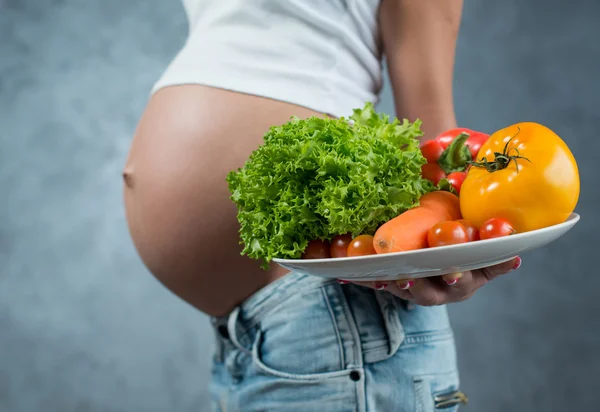 Primer plano de una linda barriga embarazada y comida saludable. fem embarazada —  Fotos de Stock
