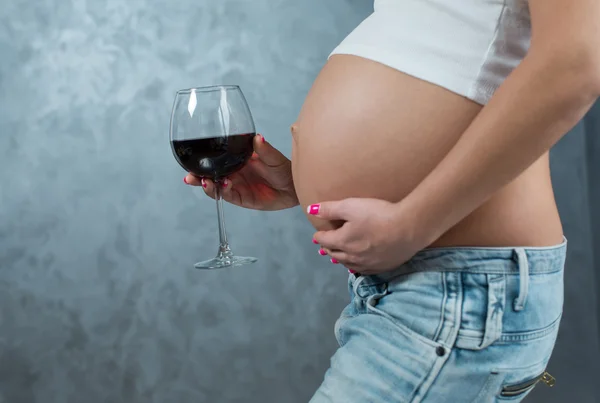 Close up of a cute pregnant belly and glass of wine. Alcohol and