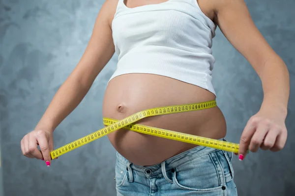 Kobieta w ciąży pomiaru brzuch żółty centymetr na szary bac — Zdjęcie stockowe