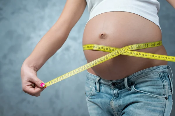 Zwangere vrouw buik meten door gele centimeter op grijze bac — Stockfoto