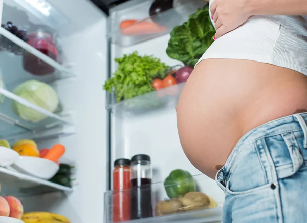 Close-up van een schattig zwangere buik buik in de buurt van de koelkast fr — Stockfoto