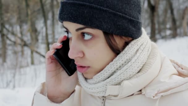 Schönes Mädchen, das im Winterpark mit dem Smartphone spricht — Stockvideo