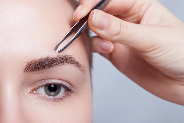 Mujer joven con el pelo corto arrancando las cejas pinzas de cerca — Foto de Stock