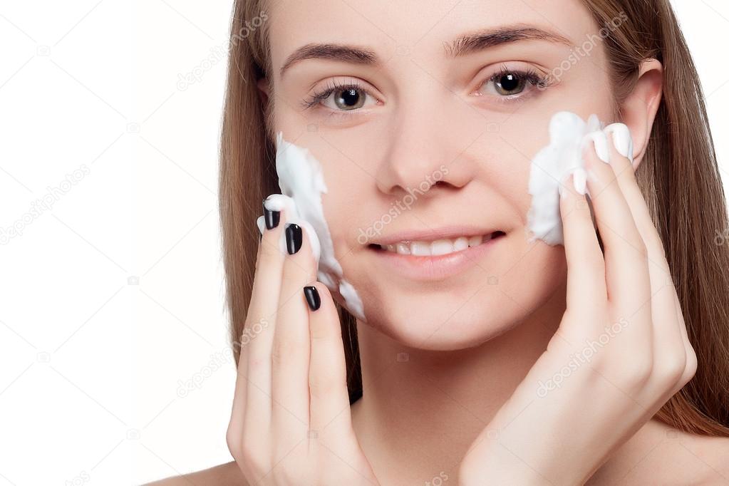 Beautiful woman cleaning face with foam treatment light background