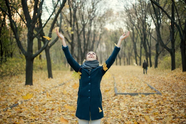 Vrouw gele bladeren in de lucht gooien — Stockfoto