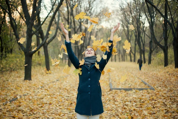 Kobieta rzuca żółte listowie w powietrzu — Zdjęcie stockowe