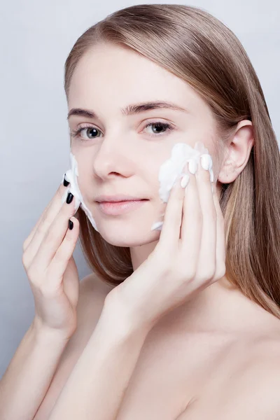 Close-up woman clears skin foam on gray background