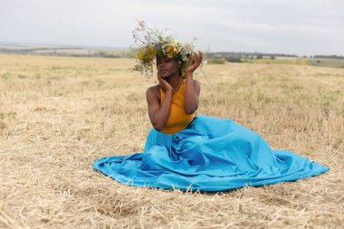 Afro-Amerikan genç bayan gün batımında dışarıda eğleniyor. Sahada gülen kız. Kır çiçekleri çelengi. Saçları örgülü güzel, Afro-Amerikan bir kadın.