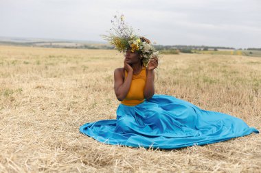 Afro-Amerikan genç bayan gün batımında dışarıda eğleniyor. Sahada gülen kız. Kır çiçekleri çelengi. Saçları örgülü güzel, Afro-Amerikan bir kadın.