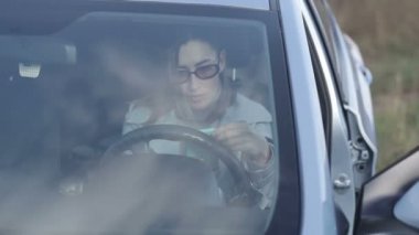 Ulaşım, araç ve teknoloji konsepti. Güzel bir genç kadın arabasında otururken akıllı telefon kullanır. Cep telefonuyla iletişim. Sosyal ağlarda sörf