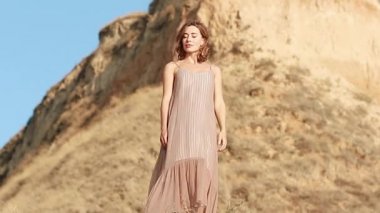 Attractive young woman on the background of a clay rock. confident woman stands, the wind blows the dress and hair. close-up. Inspiration Freedom, Travel Happiness, Evening Leisure Outdoors