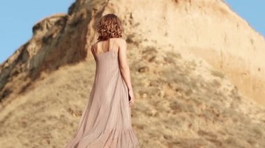 Attractive young woman on the background of a clay rock. confident woman stands, the wind blows the dress and hair. close-up. Inspiration Freedom, Travel Happiness, Evening Leisure Outdoors