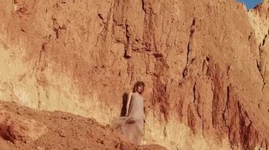 Attractive young woman on the background of a clay rock. confident woman stands, the wind blows the dress and hair. close-up. Inspiration Freedom, Travel Happiness, Evening Leisure Outdoors