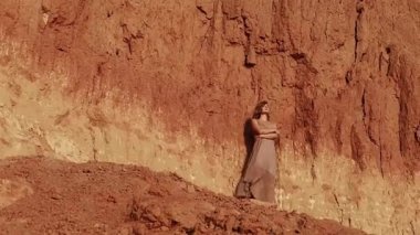Attractive young woman on the background of a clay rock. confident woman stands, the wind blows the dress and hair. close-up. Inspiration Freedom, Travel Happiness, Evening Leisure Outdoors