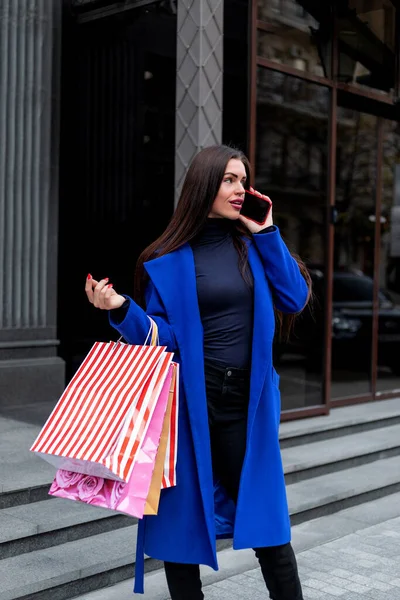 hot Sale. Beautiful young fashion woman with shopping bags near shop window calling smart phone, toned. shopping woman fun phone