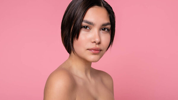 Close up face of beautiful young woman with clean perfect skin. Portrait of beauty model with natural nude make up. Spa, skin care and wellness. Pink peach coral background. 16:9 panoramic format.