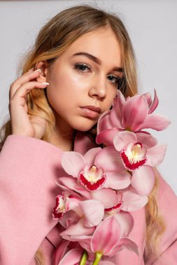 Stüdyoda gri arka planda poz veren pembe ceketli baştan çıkarıcı sarışın kadın. Pastel gündelik bahar kıyafetiyle zarif bir modelin moda portresi. Sağlıklı ciltli ve dallı güzel bir kız.