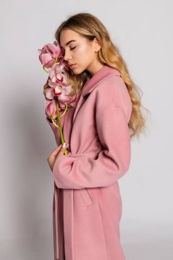 Stüdyoda gri arka planda poz veren pembe ceketli baştan çıkarıcı sarışın kadın. Pastel gündelik bahar kıyafetiyle zarif bir modelin moda portresi. Sağlıklı ciltli ve dallı güzel bir kız.