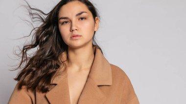 Gri arka planda stüdyoda poz veren kahverengi ceketli baştan çıkarıcı sarışın kadın. Pastel gündelik bahar kıyafetleri içinde zarif bir model. Sağlıklı ciltli ve dallı güzel bir kız. 16: 9 panoramik biçimi.