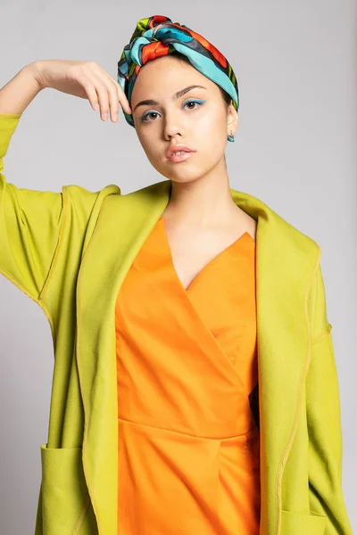 明るいメイクとファッショナブルなスカーフを持つ若い女性の肖像画 光の背景 美しさ ファッション メイクのコンセプト 明るい緑のコートに明るいオレンジのドレスを着た女の子 — ストック写真