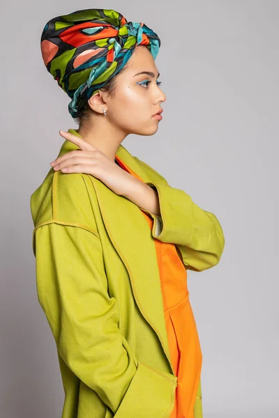 Portrait of a young woman with bright makeup and a fashionable headscarf. Light background. Beauty, fashion, makeup concept. girl in a bright green coat, bright orange dress.