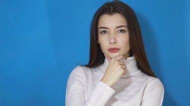 Zeki esmer kadın ciddi bir plan düşünüyor, kafasındaki problemi çözüyor ve onaylayarak başını sallıyor, zekice bir fikir üzerinde düşünüyor, düşünüp taşınıyor. Mavi arka planda kapalı stüdyo çekimleri