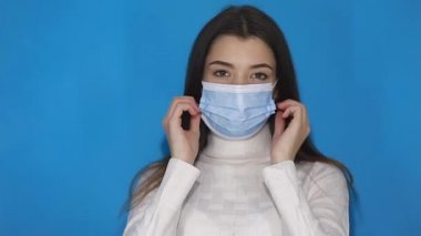 Solunum enfeksiyonunu önlemek için yüz hijyenik maskesi takan beyaz kazaklı bir kız grip olarak hava salgını, bulaşıcı koronavirüs. Mavi arka planda kapalı stüdyo çekimleri